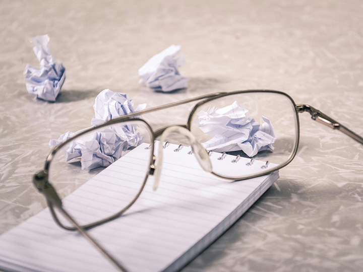 Brille auf einem Notizblock liegend, daneben zerknüllte Zettel