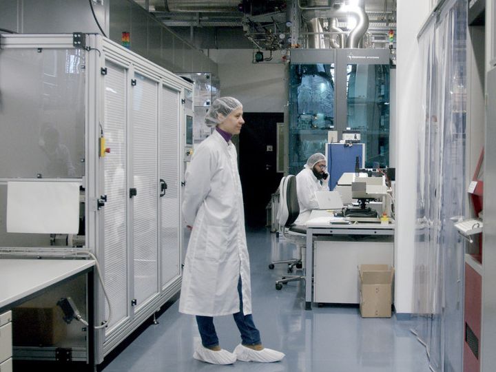 zwei Personen mit Laborkittel und Haarnetz in einer steril wirkenden technischen Anlage