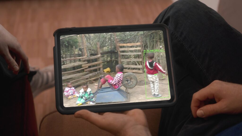 Zwei Hände halten ein Tablet, auf dem verschiedene Kinder beim Spielen gezeigt werden